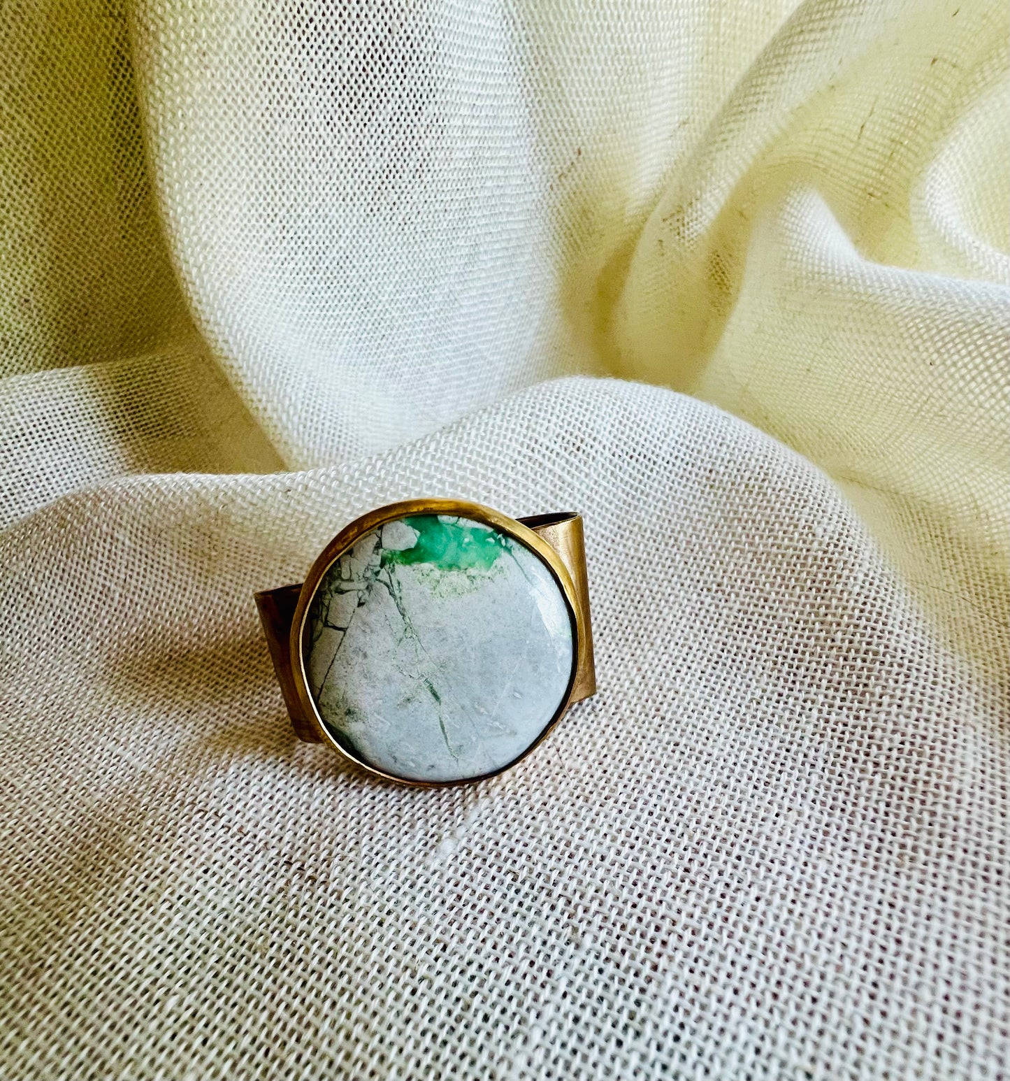 Wild rag bronze bandana slide with green variscite stone. Displayed on cream linen background.