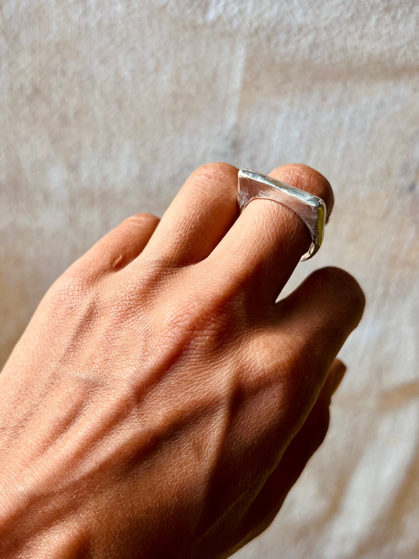 Hand model with sculpted thin signet ring in silver displayed with cream background. Lost wax ring.