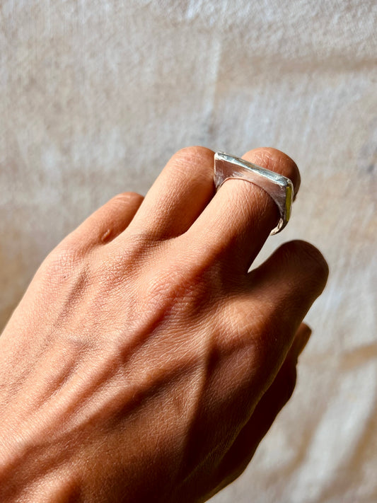 Hand model with sculpted thin signet ring in silver displayed with cream background. Lost wax ring.