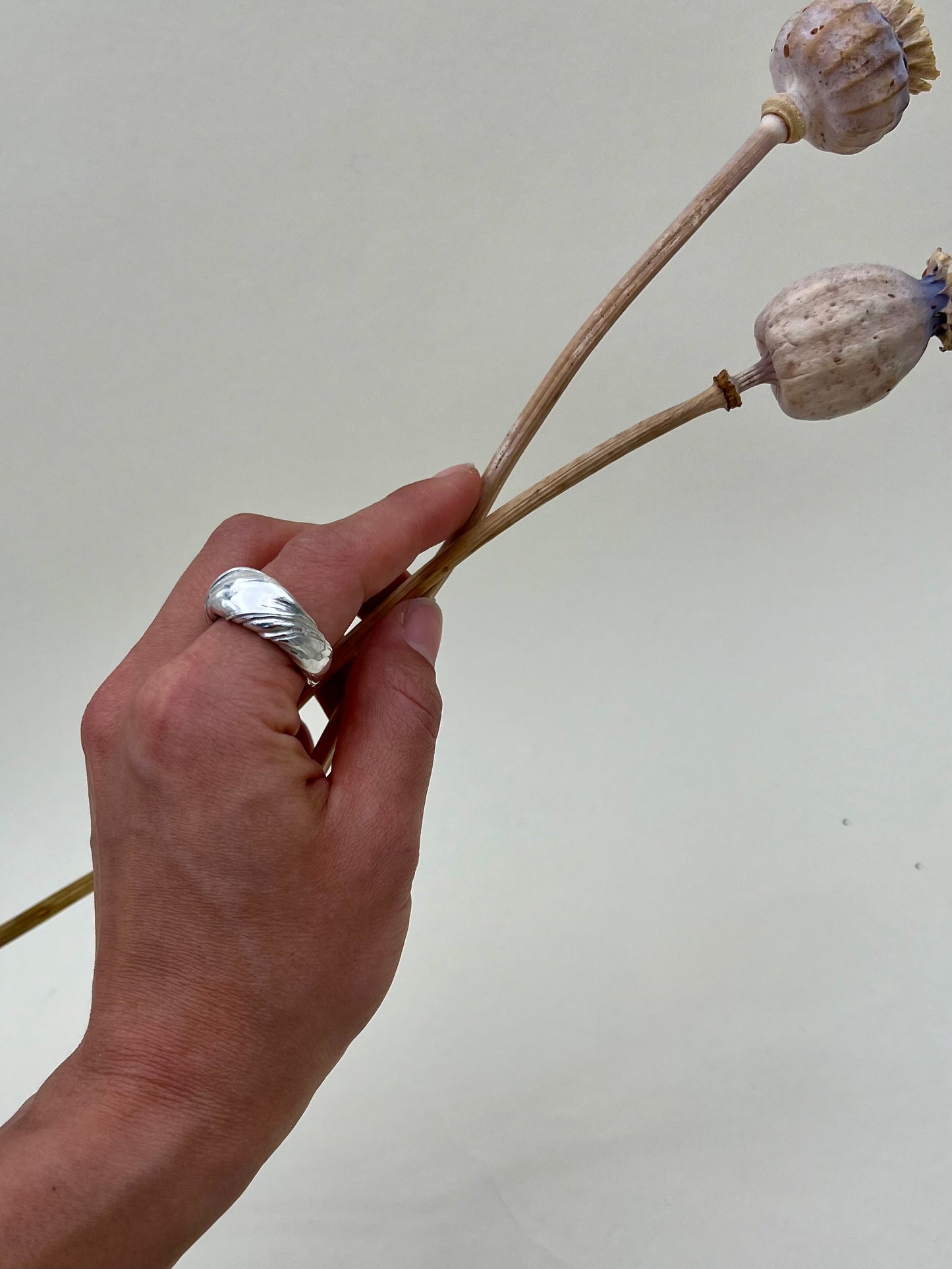 Silver sculptural ring crafted using the Mitsuro Hikime technique by Soul Full Studio. Hand model with white background and dried poppies.