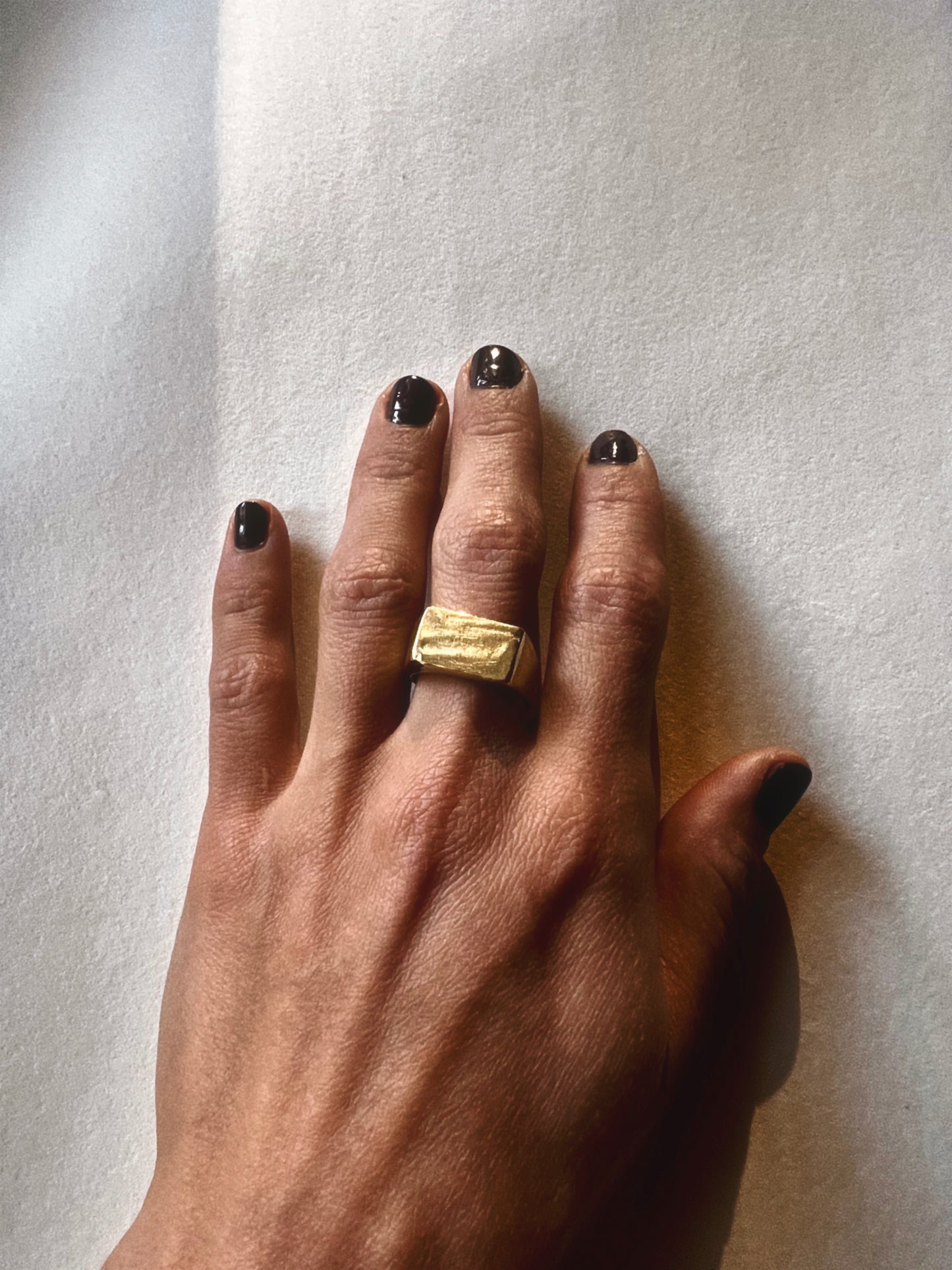 Hand wearing a yellow brass horizon ring. Displayed on beige background with shadows.
