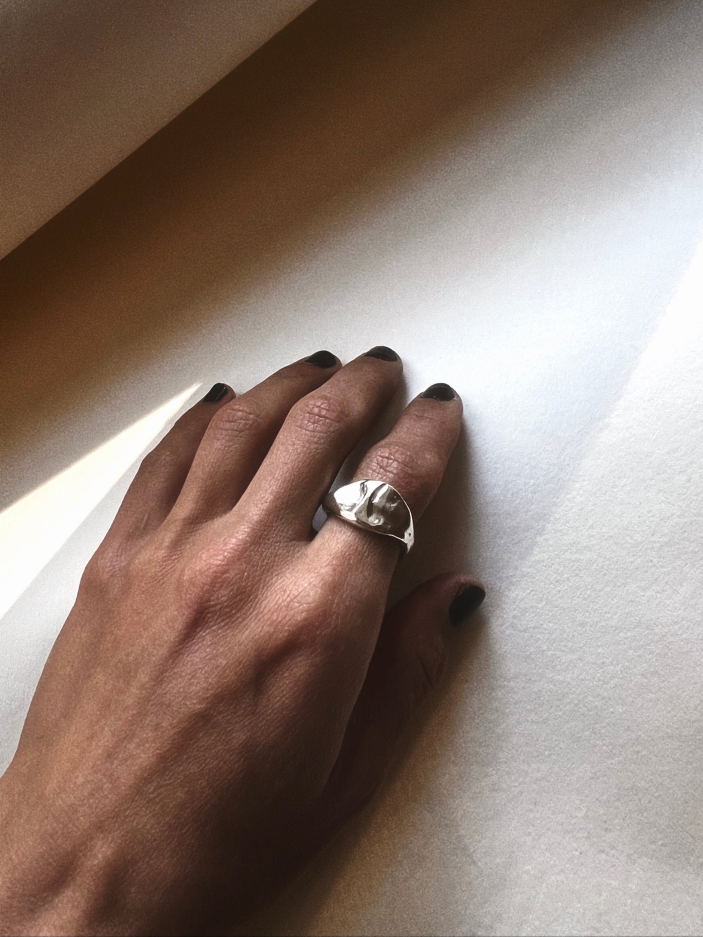 Hand wearing a silver ring on a light-colored surface