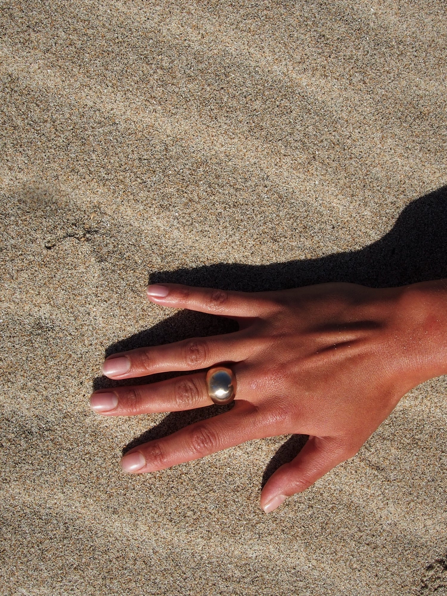 Handcrafted in a dome ring shape, this creation by Soulfull Studio is a product of intricate artistry. Utilizing lost wax casting techniques with recycled bronze, it derives its inspiration from the allure of natural elements. Hand model wearing sol ring with sand background.