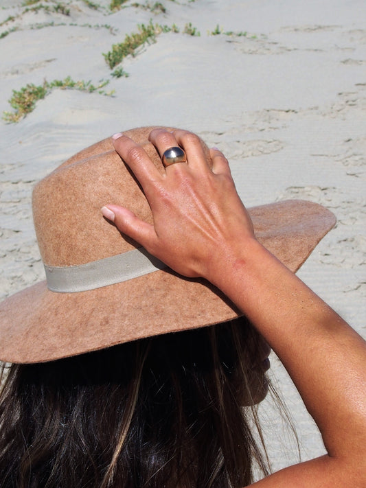 Handcrafted in a dome ring shape, this creation by Soulfull Studio is a product of intricate artistry. Utilizing lost wax casting techniques with recycled bronze, it derives its inspiration from the allure of natural elements. Jewelry for the wild ones. Model at beach with sun hat. 
