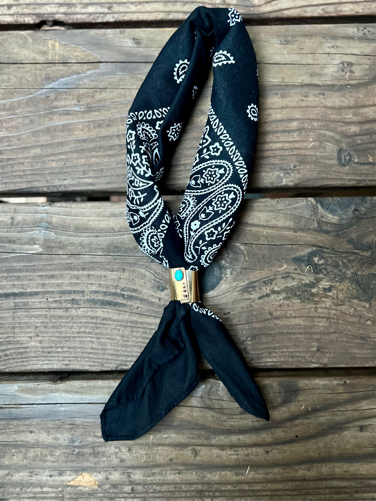 Wild rag bronze bandana slide with turquoise stone. Displayed with black bandana on wooden back group. 