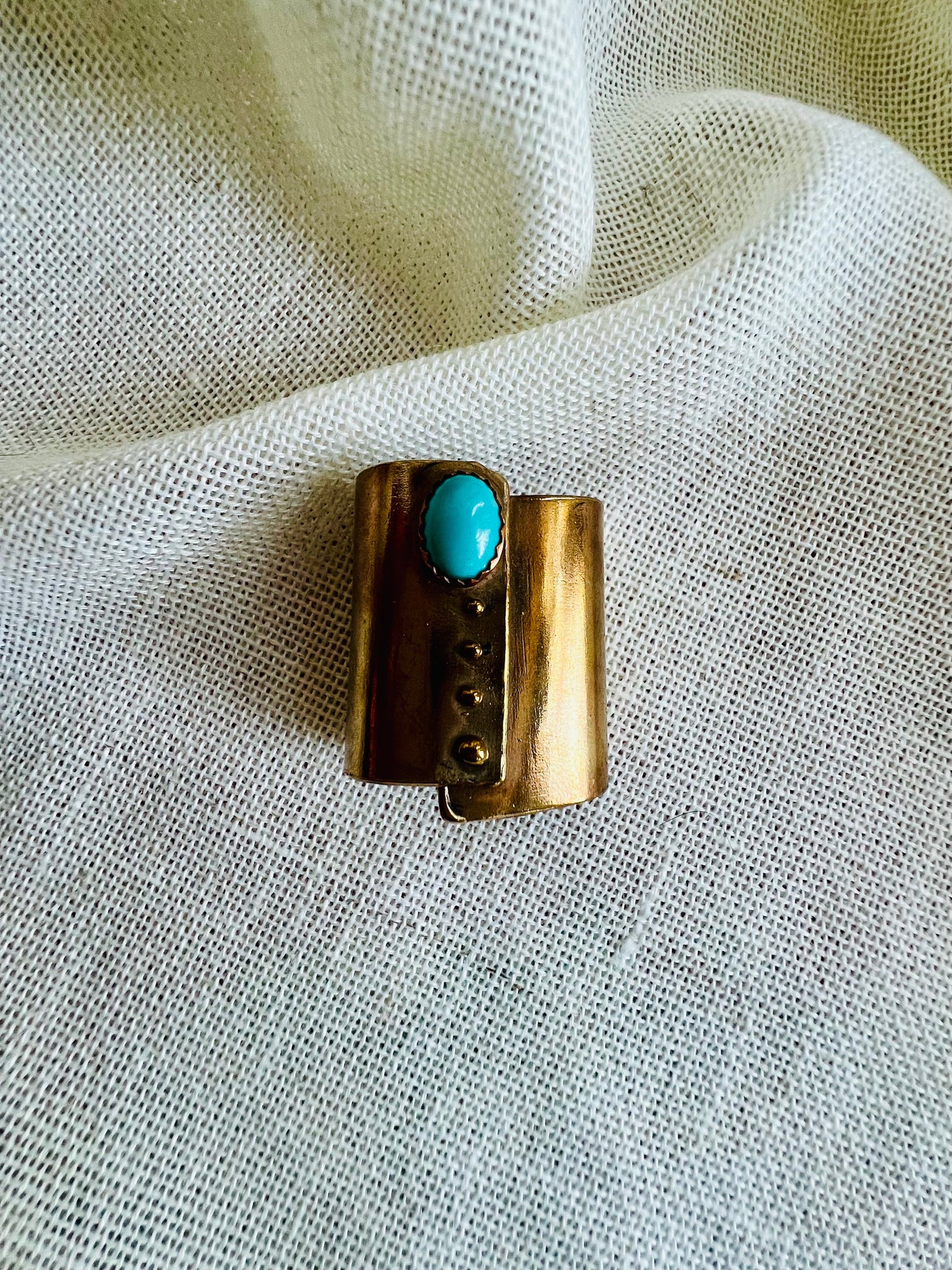 Wild rag bronze bandana slide with turquoise stone. Displayed on cream linen background. 