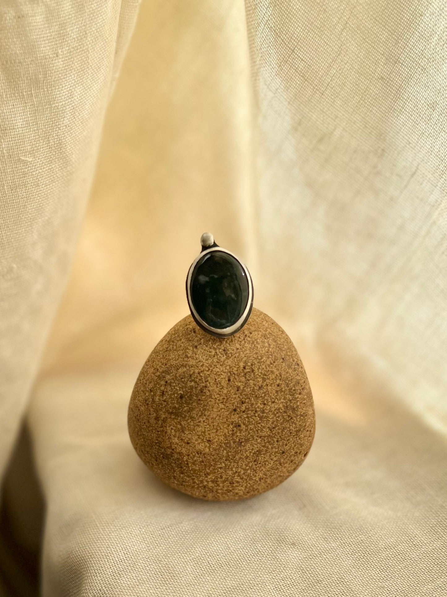 Green moss agate set in sterling silver. Displayed on rock prop with cream linen background. Handmade from soul full studio using metal smithing techniques. 