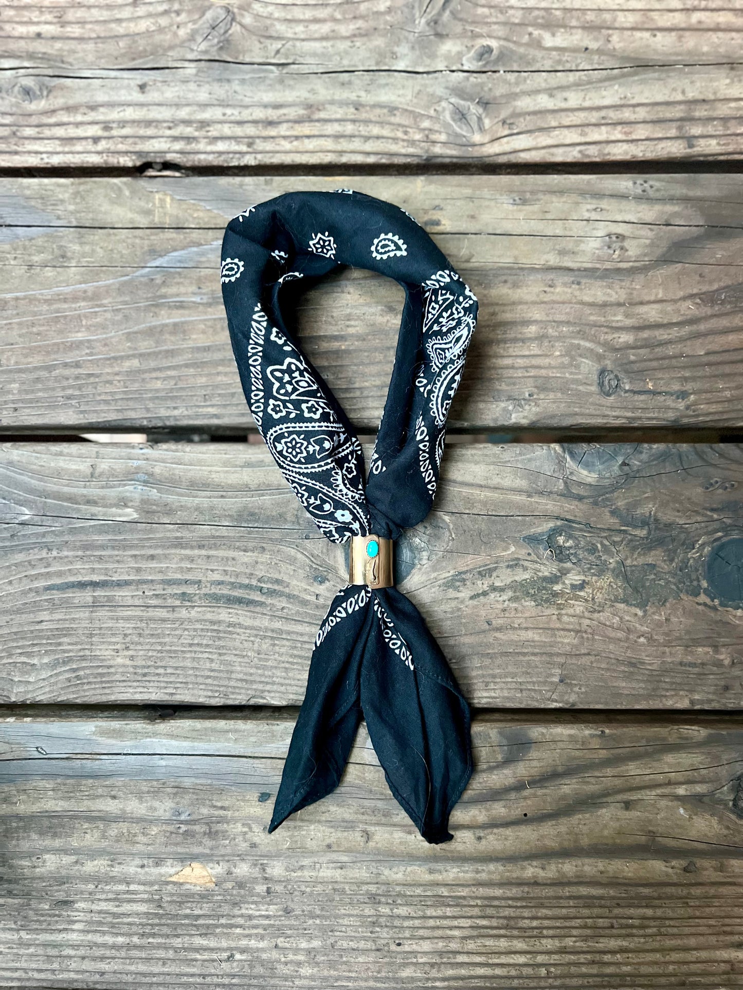 Wild rag bronze bandana slide with turquoise stone. Displayed with black bandana on wooden back group. 