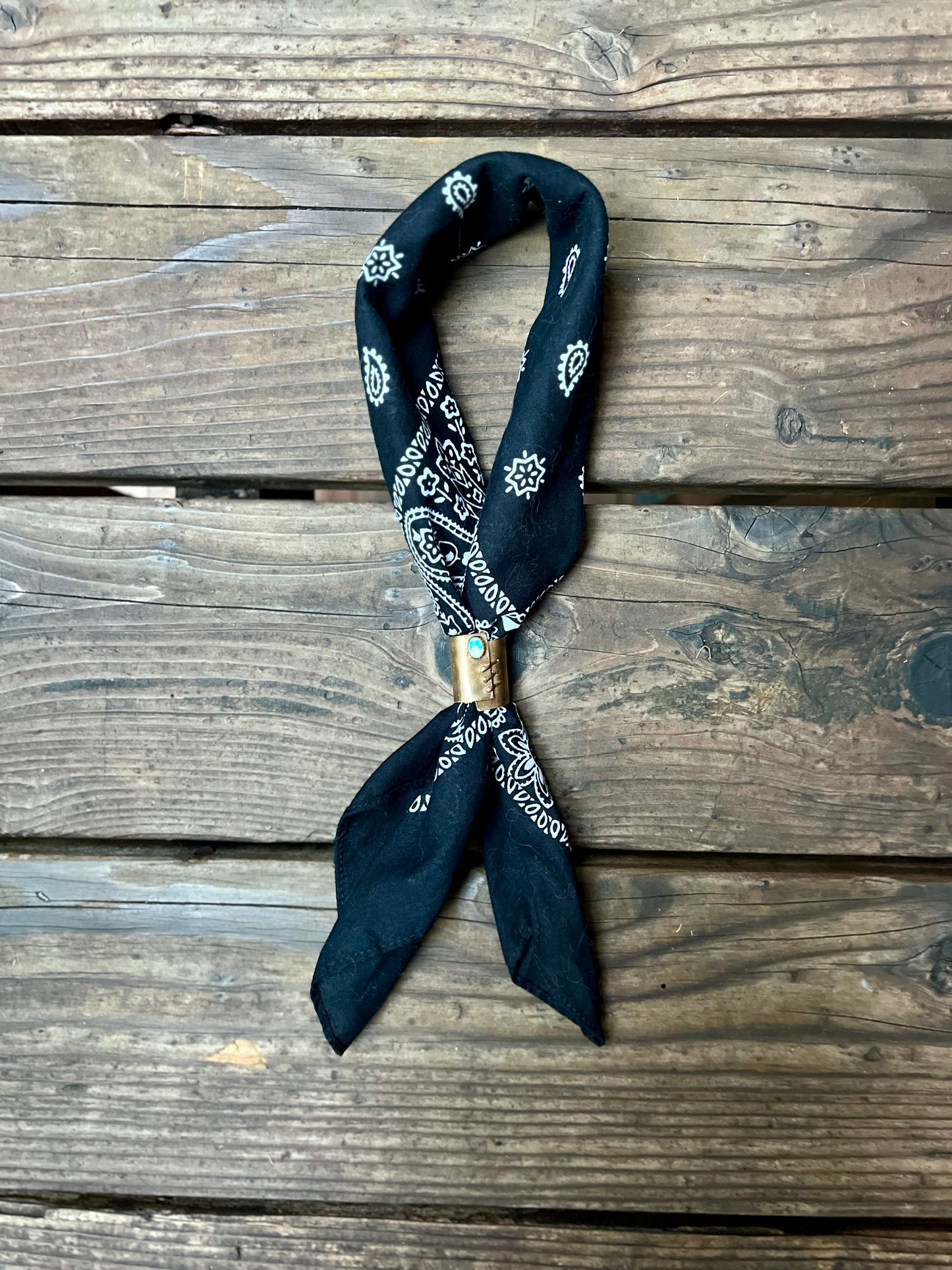 Wild rag bronze bandana slide with turquoise stone. Displayed with black bandana on wooden back group. 