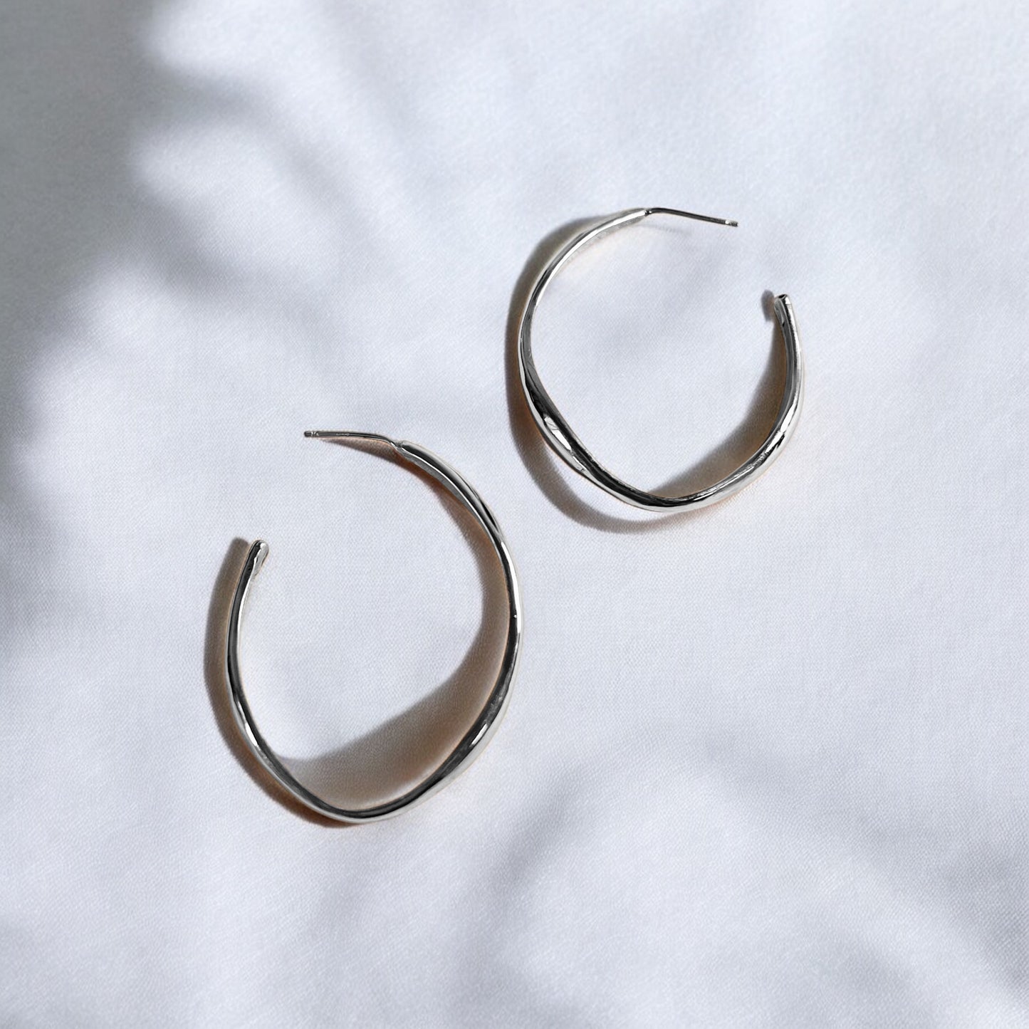 Soul full studio medium silver oval hoops displayed on linen background with natural shadows.