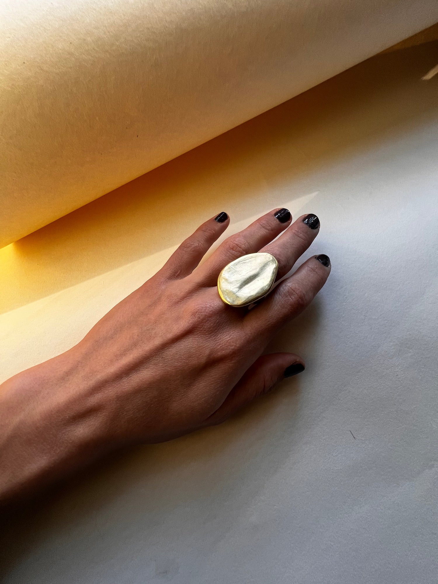 Hand with between earth and sky ring. displayed on cream background with light and shadows. 
