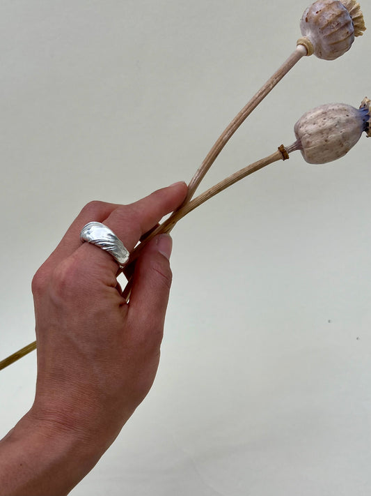 Silver sculptural ring crafted using the Mitsuro Hikime technique by Soul Full Studio. Hand model with white background and dried poppies. 