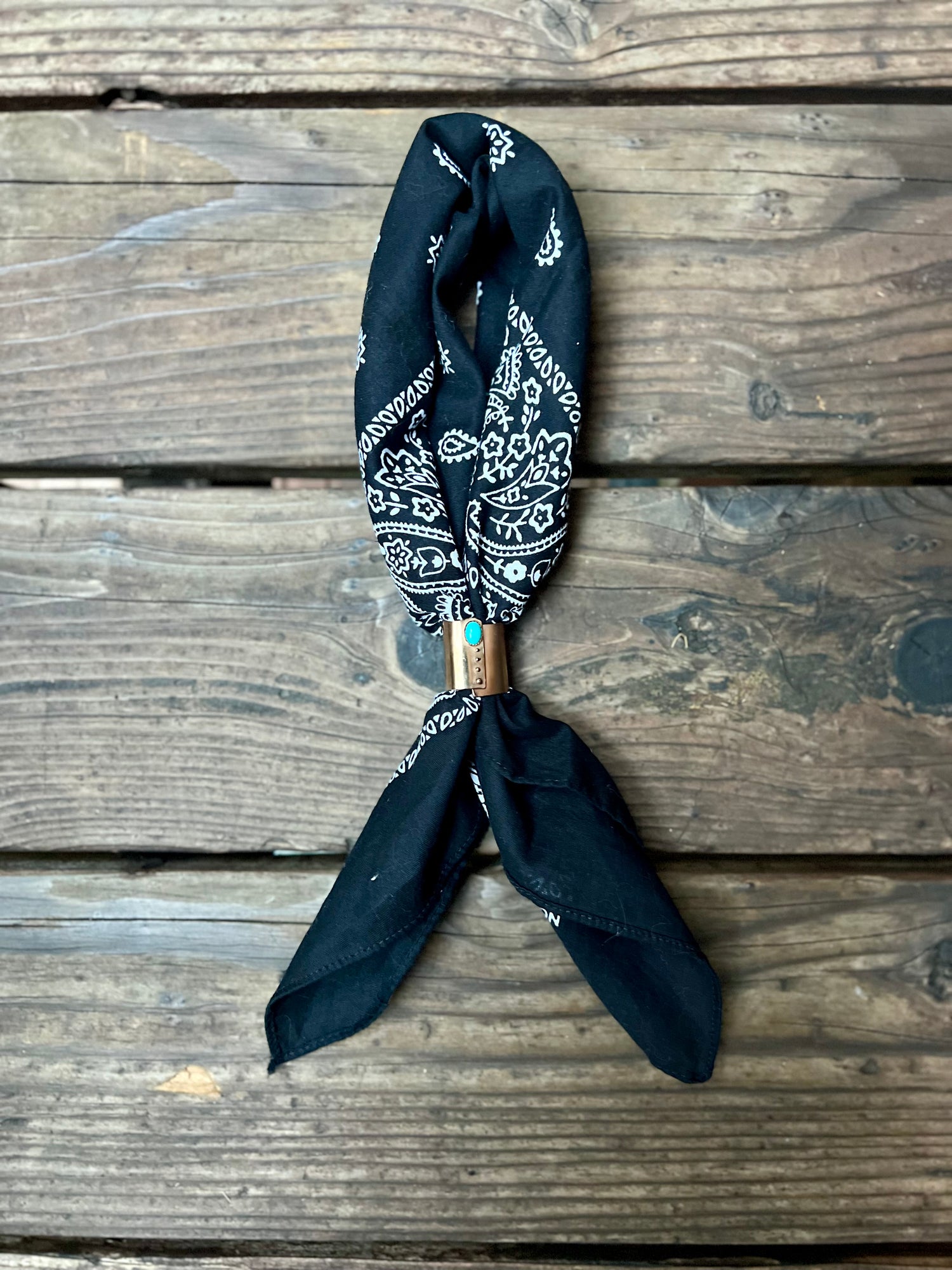 Wild rag bronze bandana slide with turquoise stone. Displayed with black bandana on wooden back group. 