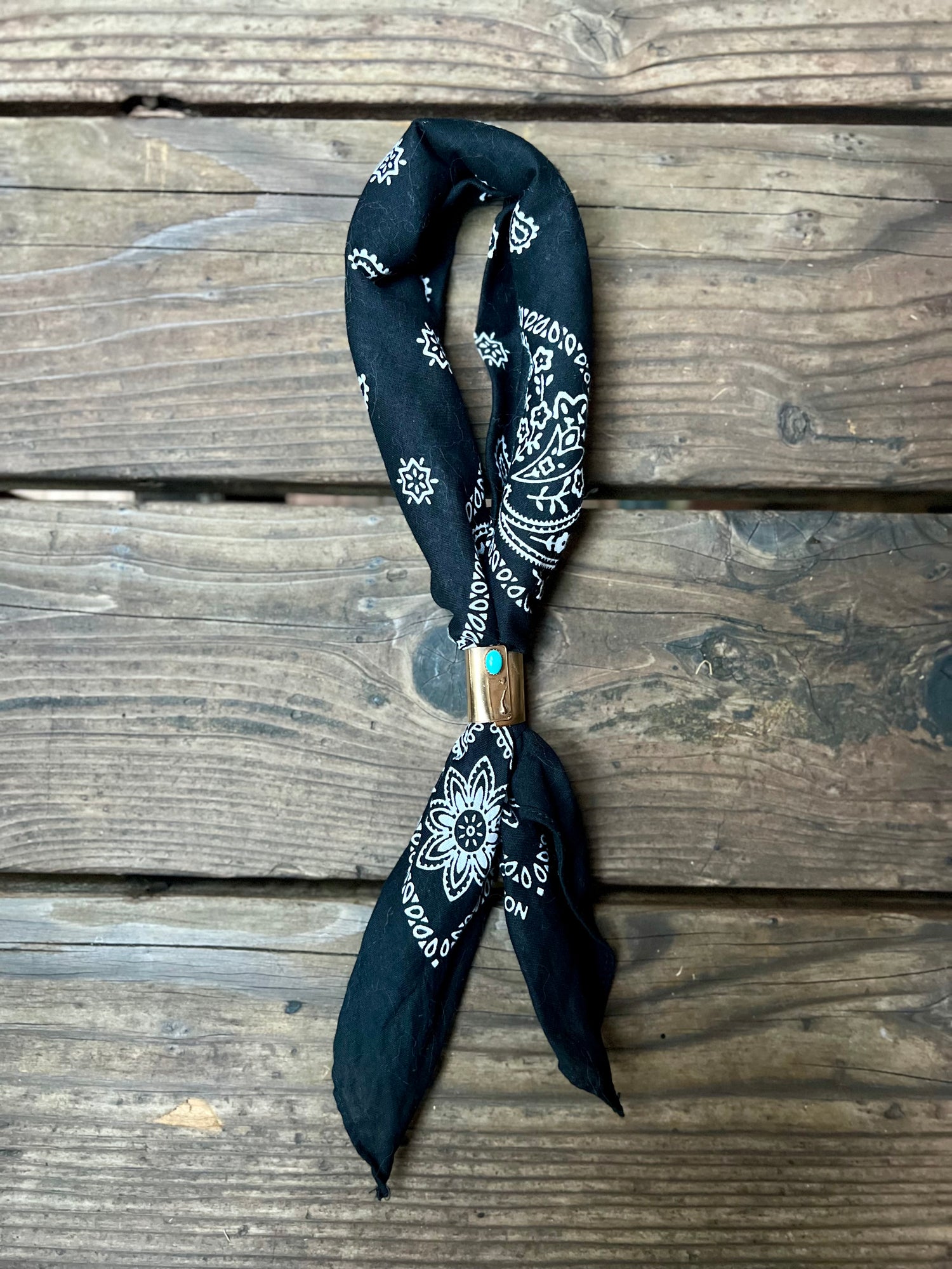 Wild rag bronze bandana slide with turquoise stone. Displayed with black bandana on wooden back group. 