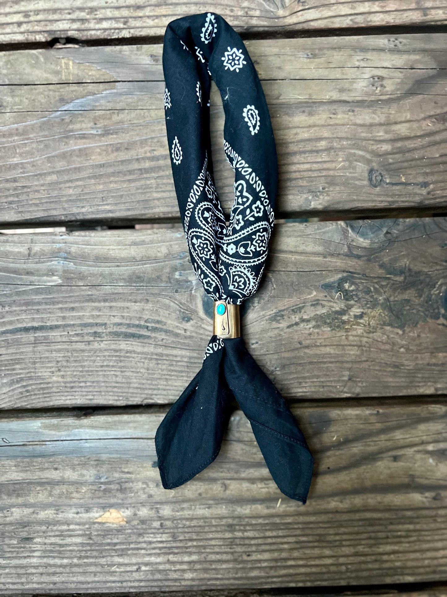 Wild rag bronze bandana slide with turquoise stone. Displayed with black bandana on wooden back group. 