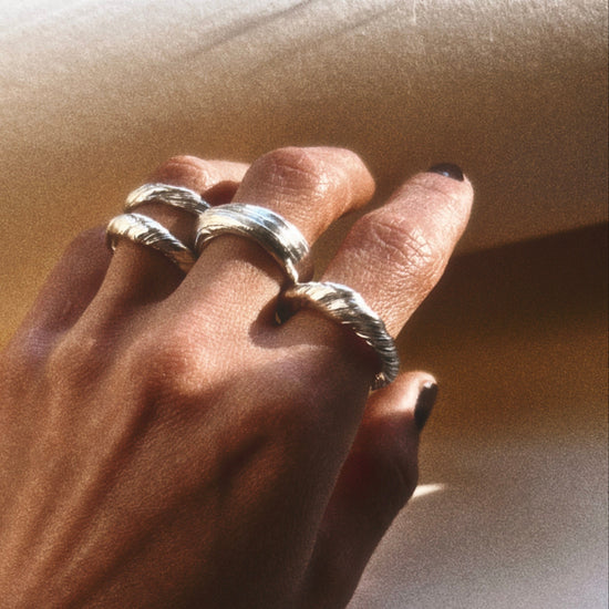 Hand wearing multiple silver rings on a neutral background
