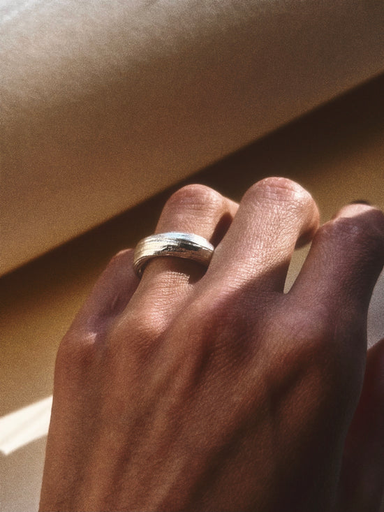 Hand wearing a silver mitsuro hikime ring on a beige background