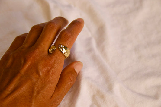 A close-up of a hand wearing tide keeper ring against a soft, off-white fabric background.
