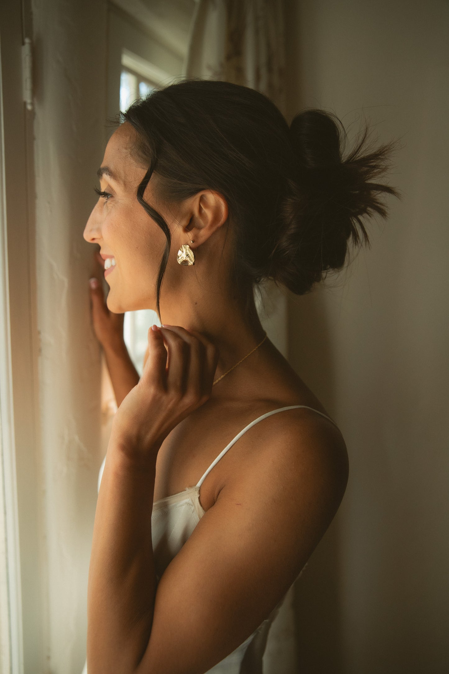 Woman adjusting her bridal earrings in a softly lit room