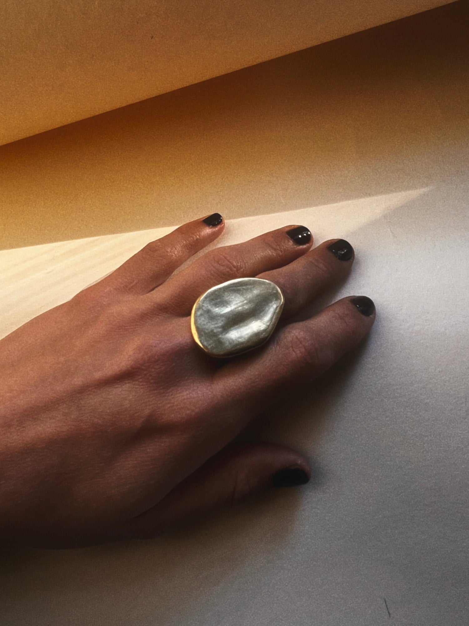Hand wearing a large ring on a neutral background with shadows