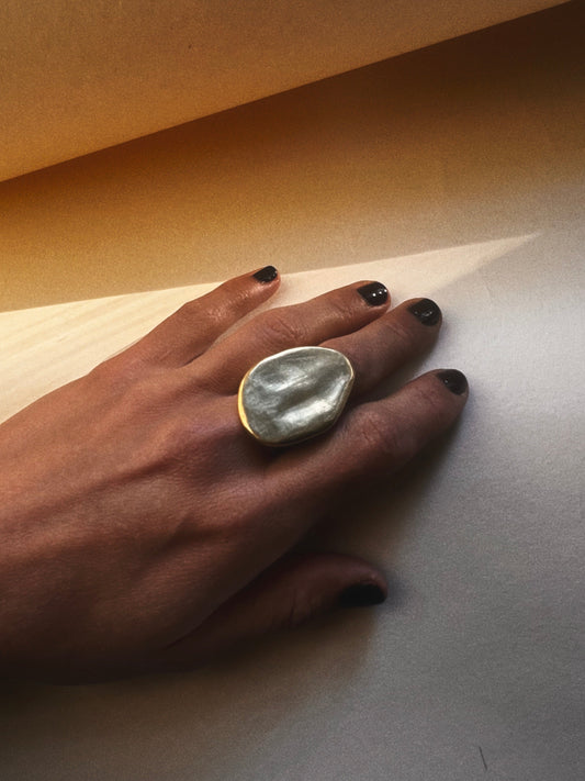 Hand wearing a large ring on a neutral background with shadows
