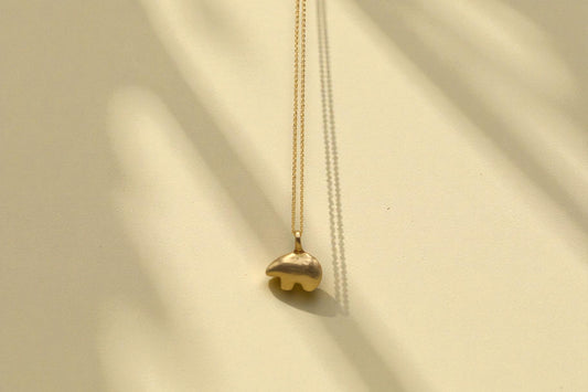 Osos bear necklace with gold chain on light background with shadows. 
