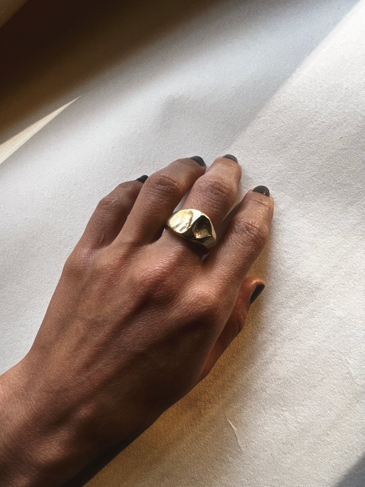 Hand wearing a gold ring on a light background with shadow