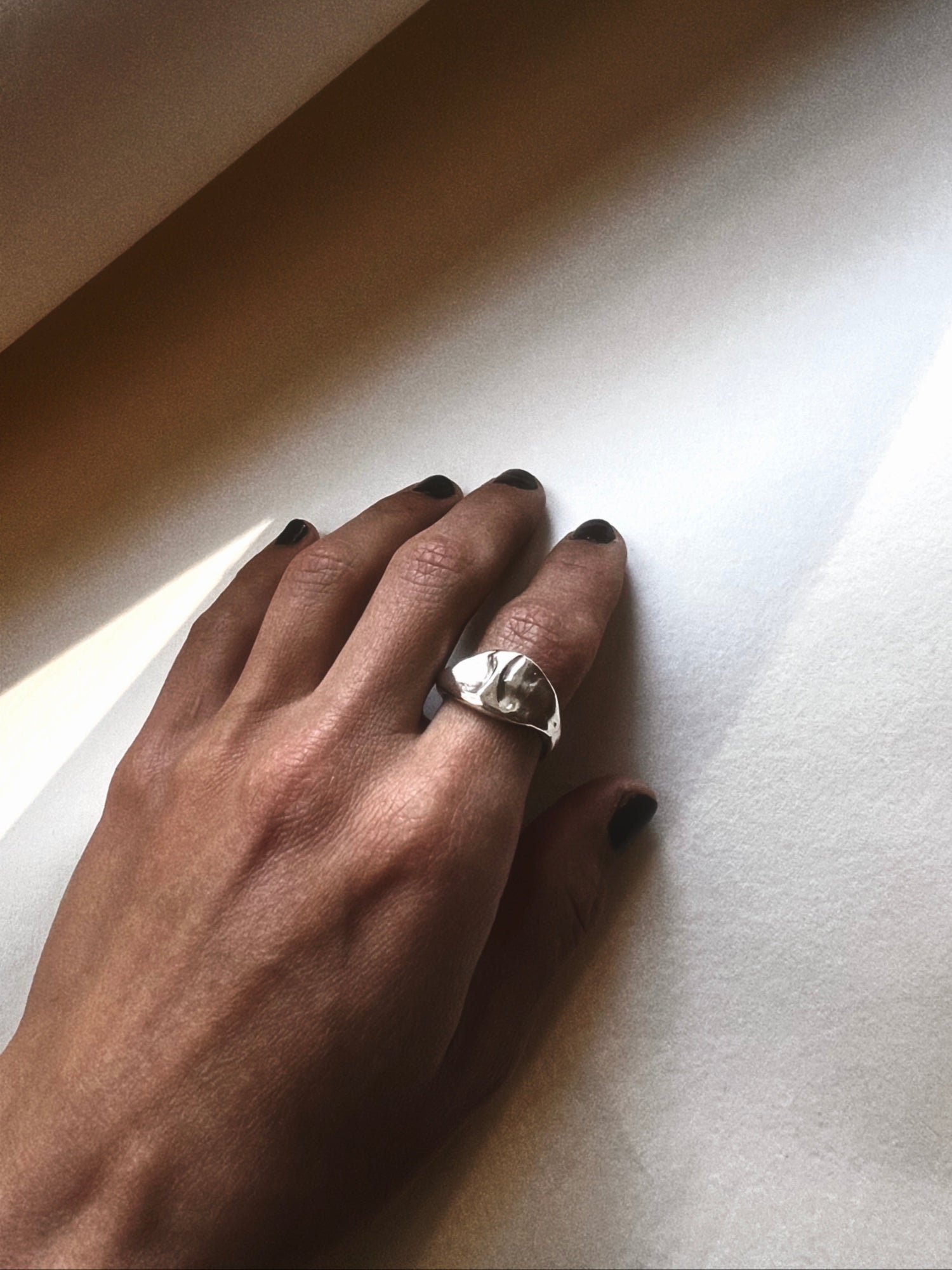 Hand wearing a silver ring on a light-colored surface