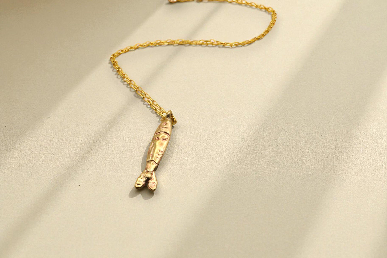 Yellow brass tin fish necklace with gold chain on light background with shadows. 