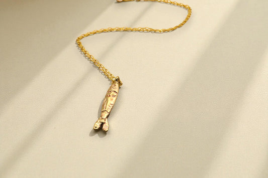Yellow brass tin fish necklace with gold chain on light background with shadows. 
