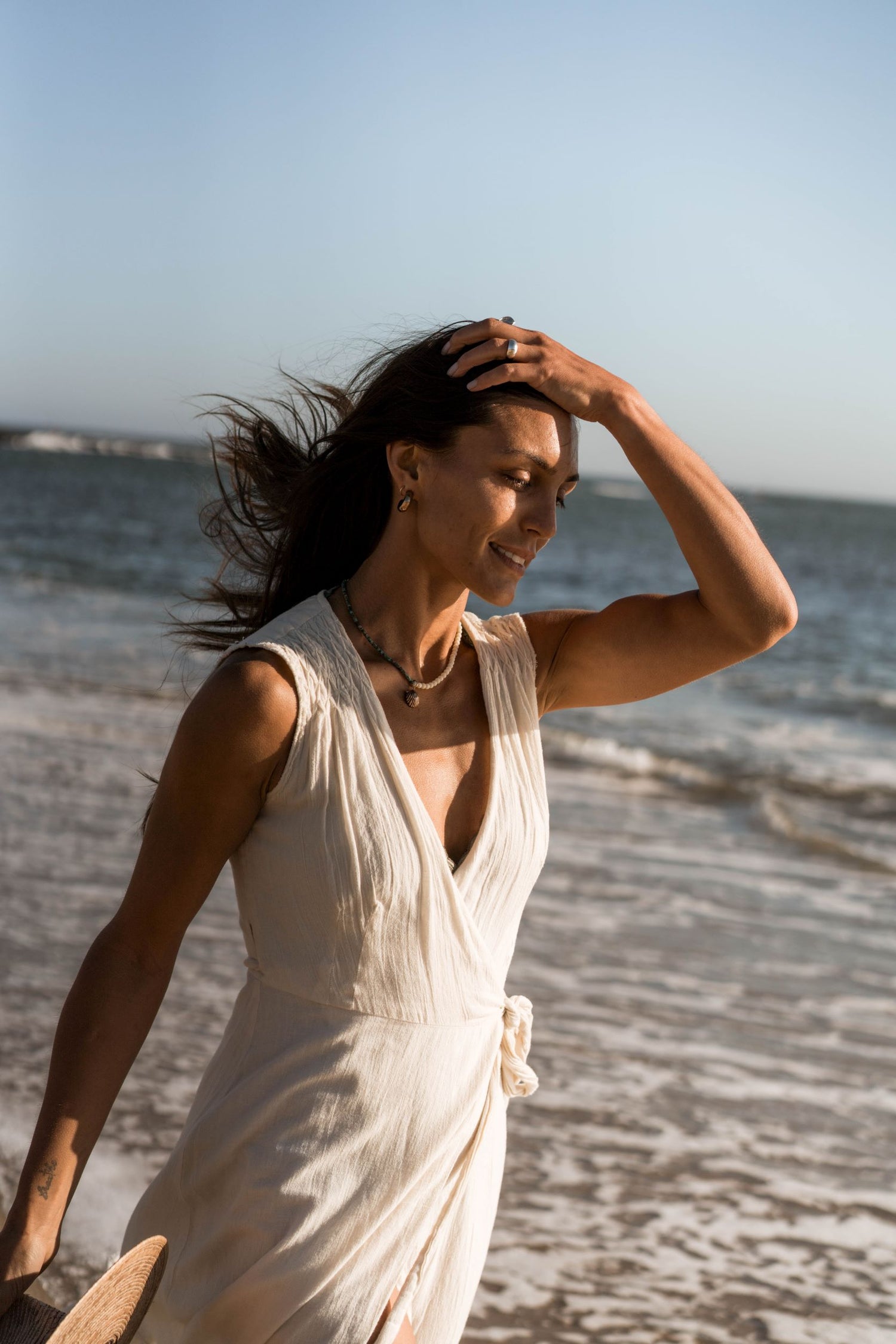 Handcrafted sculpted earrings, meticulously carved using the lost wax casting technique and crafted from recycled bronze. Created by Soulfull Studio. Jewelry for the wild ones. Model wearing roca earrings in white dress at beach. 